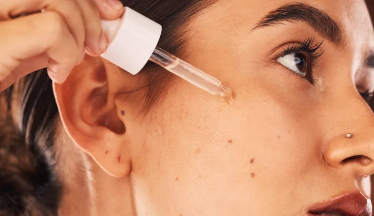 A woman applies a serum to her cheek.